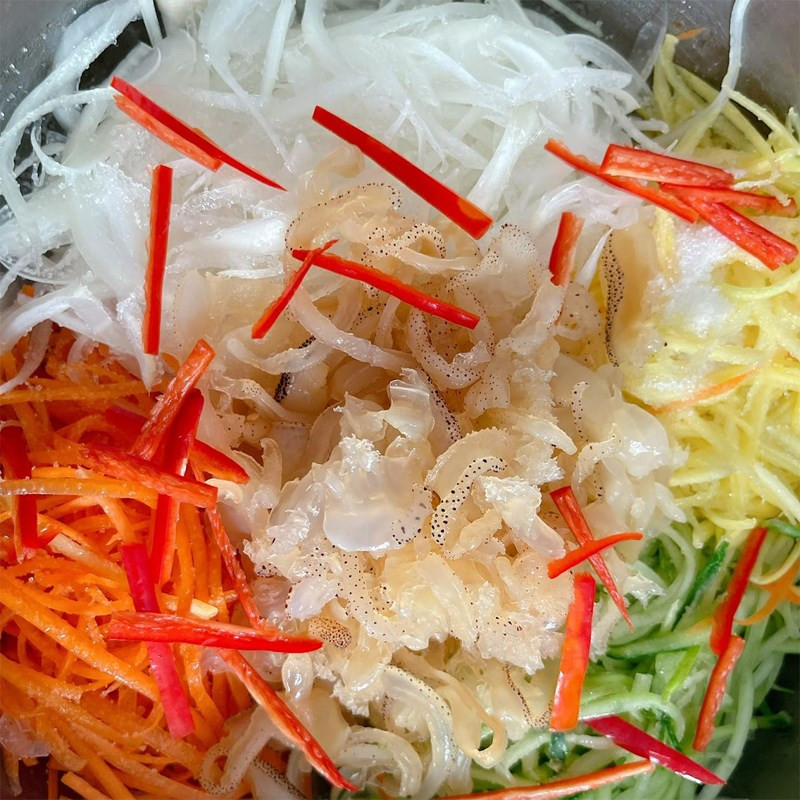 A large bowl with jellyfish, celery, carrots, and onions being mixed with the salad dressing.